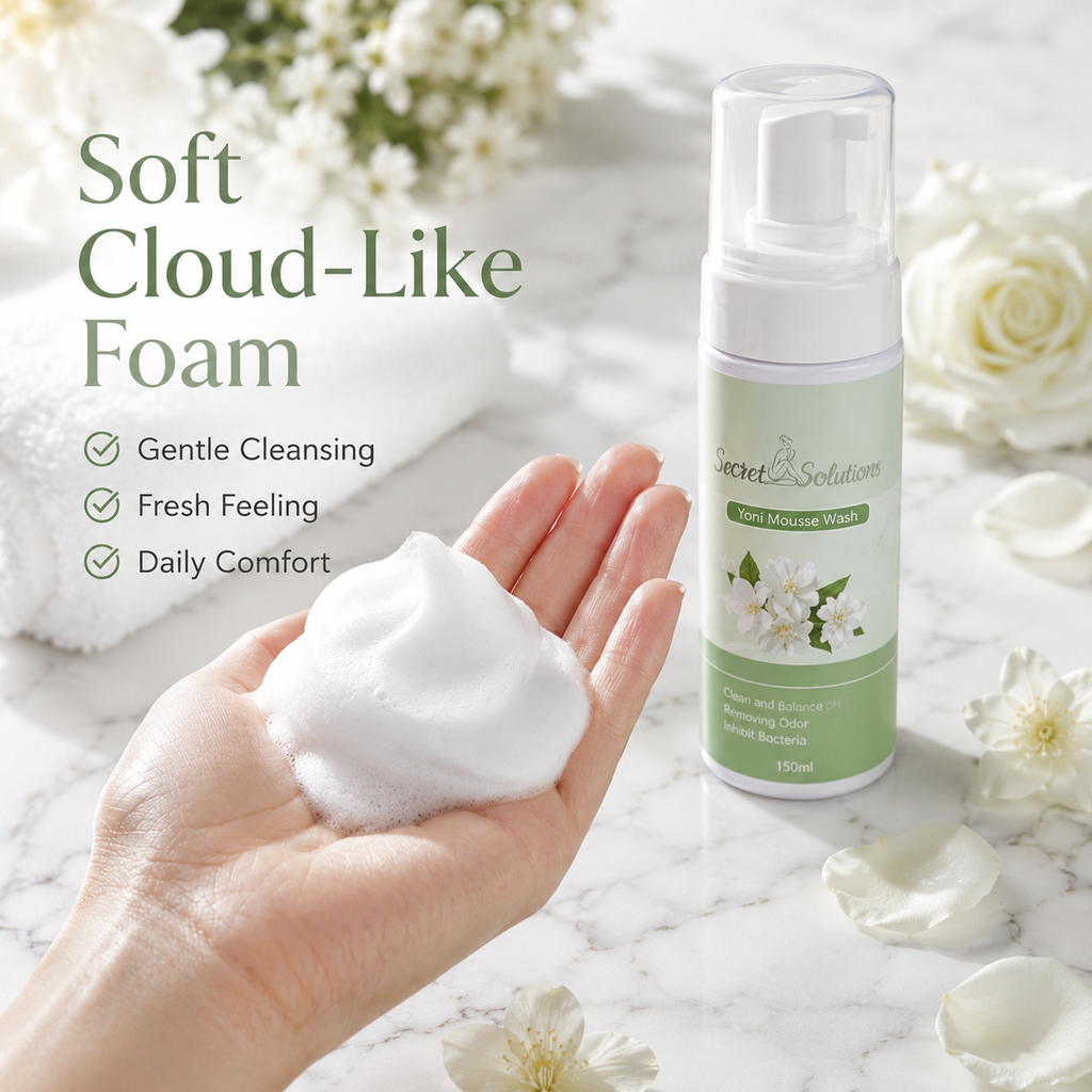 A hand holds a dollop of soft white foam next to a bottle of Scent & Solution Toner Moisture Wash on a marble surface with white flowers and petals.