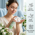 A woman in a cream robe applies a white foam pump from a green and white bottle labeled 'Flora Geladina' in a bright, spa-like setting with white flowers. A vertical text panel on the right lists product benefits: Gentle Daily Care, Fresh Feeling, and Skin Friendly Formula.