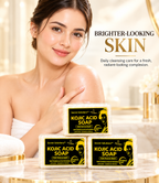 Three bars of Secret Solutions Kojic Acid Soap are displayed on a marble countertop in a bright bathroom setting, with a woman holding one bar behind them. The soap packaging is black and yellow, and the image includes promotional text on the right.